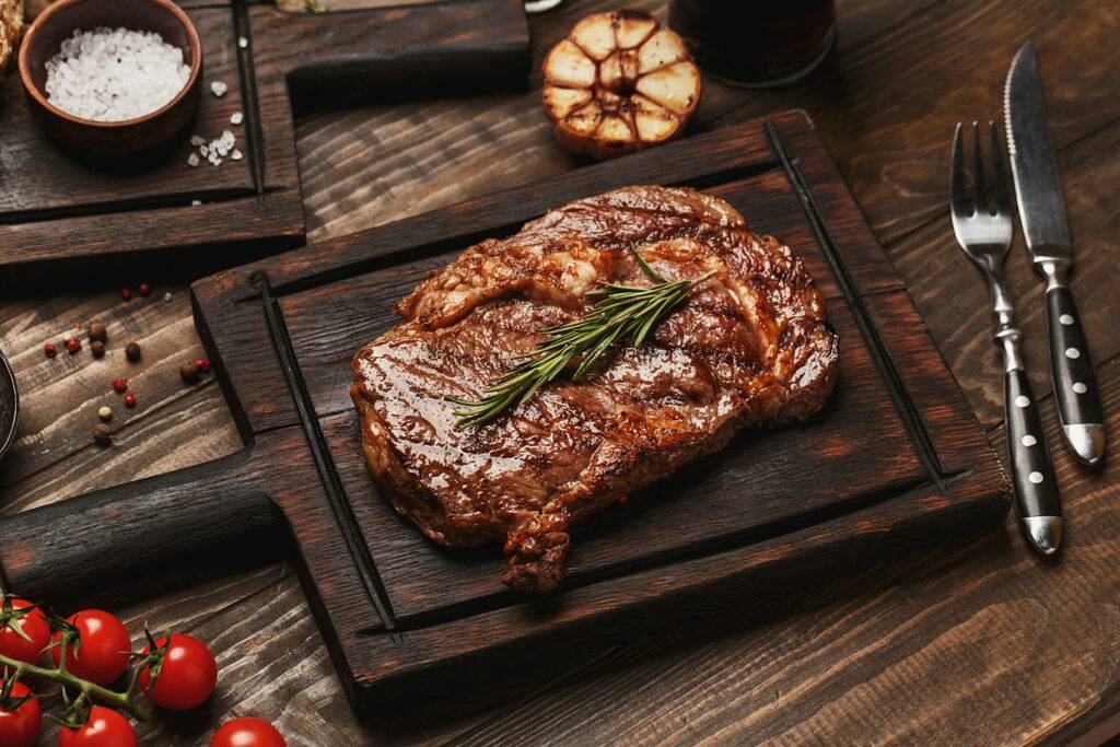 grilled ribeye beef steak served on wooden board with rosemary